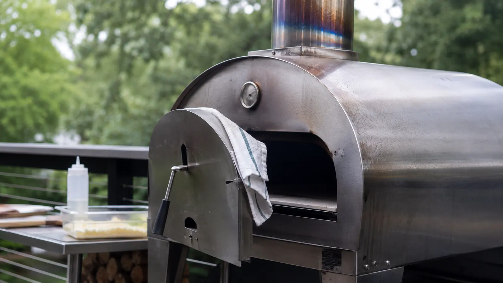 Close midday shot of the BIG HORN pizza oven's stainless exterior showing light heat discoloration near the chimney and a worn door hinge
