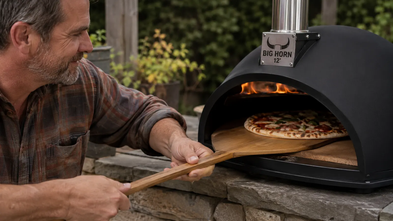 Hand sliding a pizza peel with a raw dough round into the BIG HORN oven's open mouth