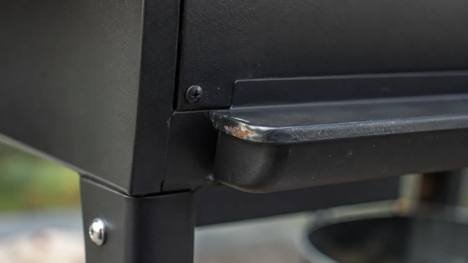 Macro close-up of a small rust spot forming near the smoker's grease tray edge
