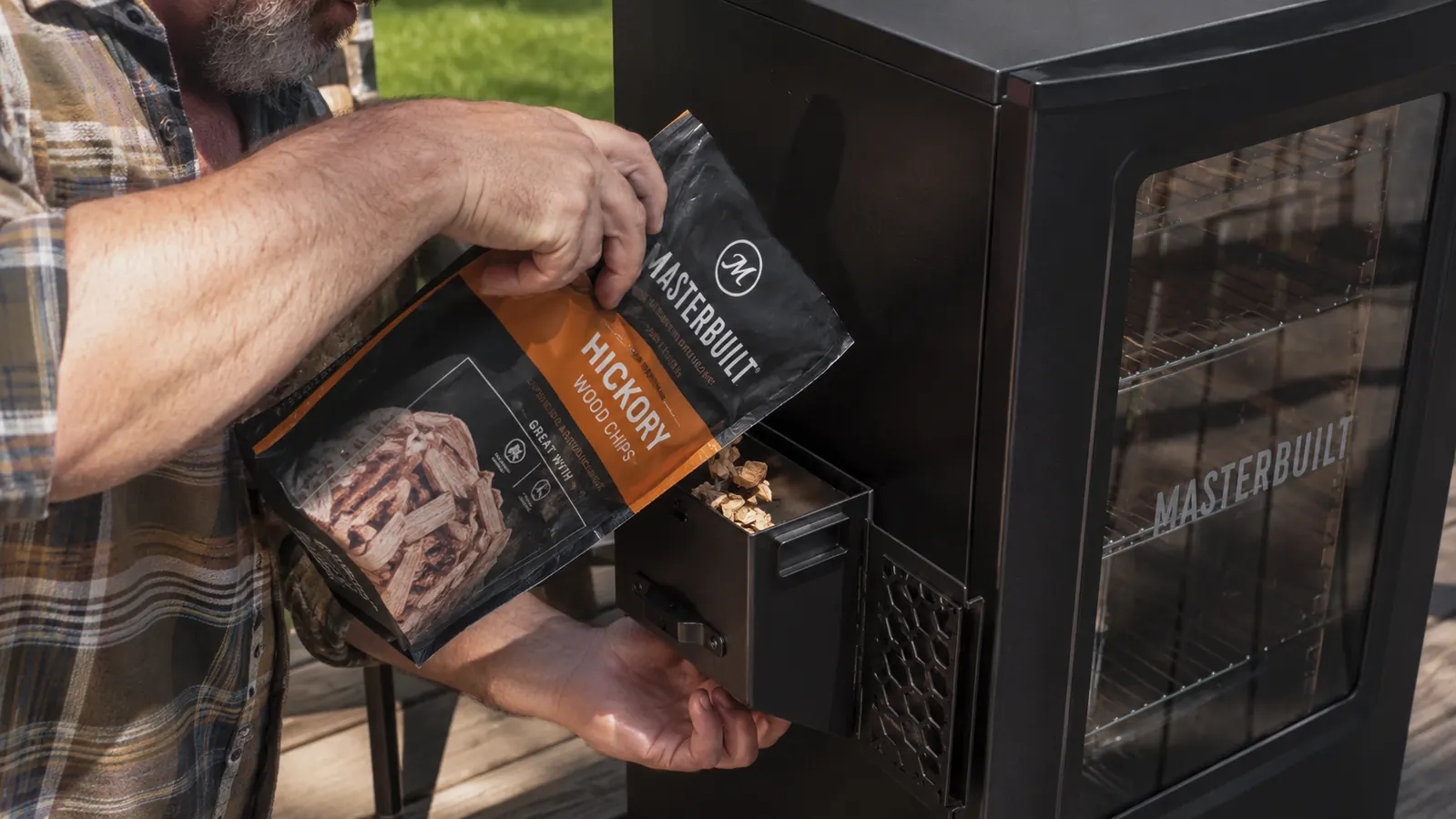 Hand pouring wood chips into the side loading tray of the Masterbuilt electric smoker